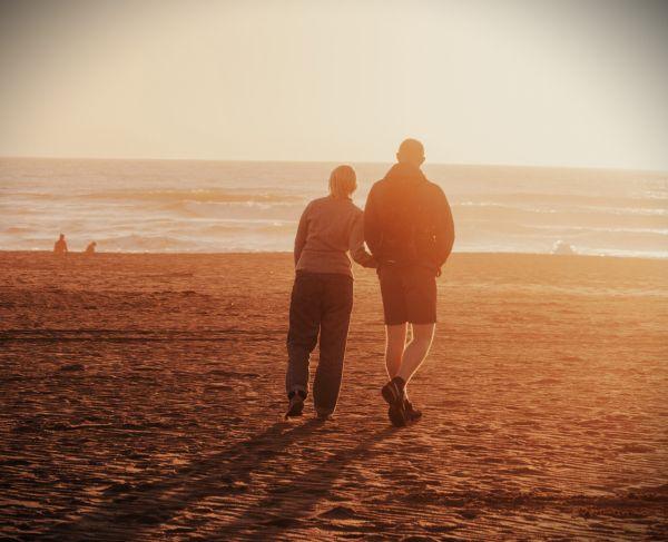 man and woman walking across a beach at dusk the man supports the woman physically as they walk