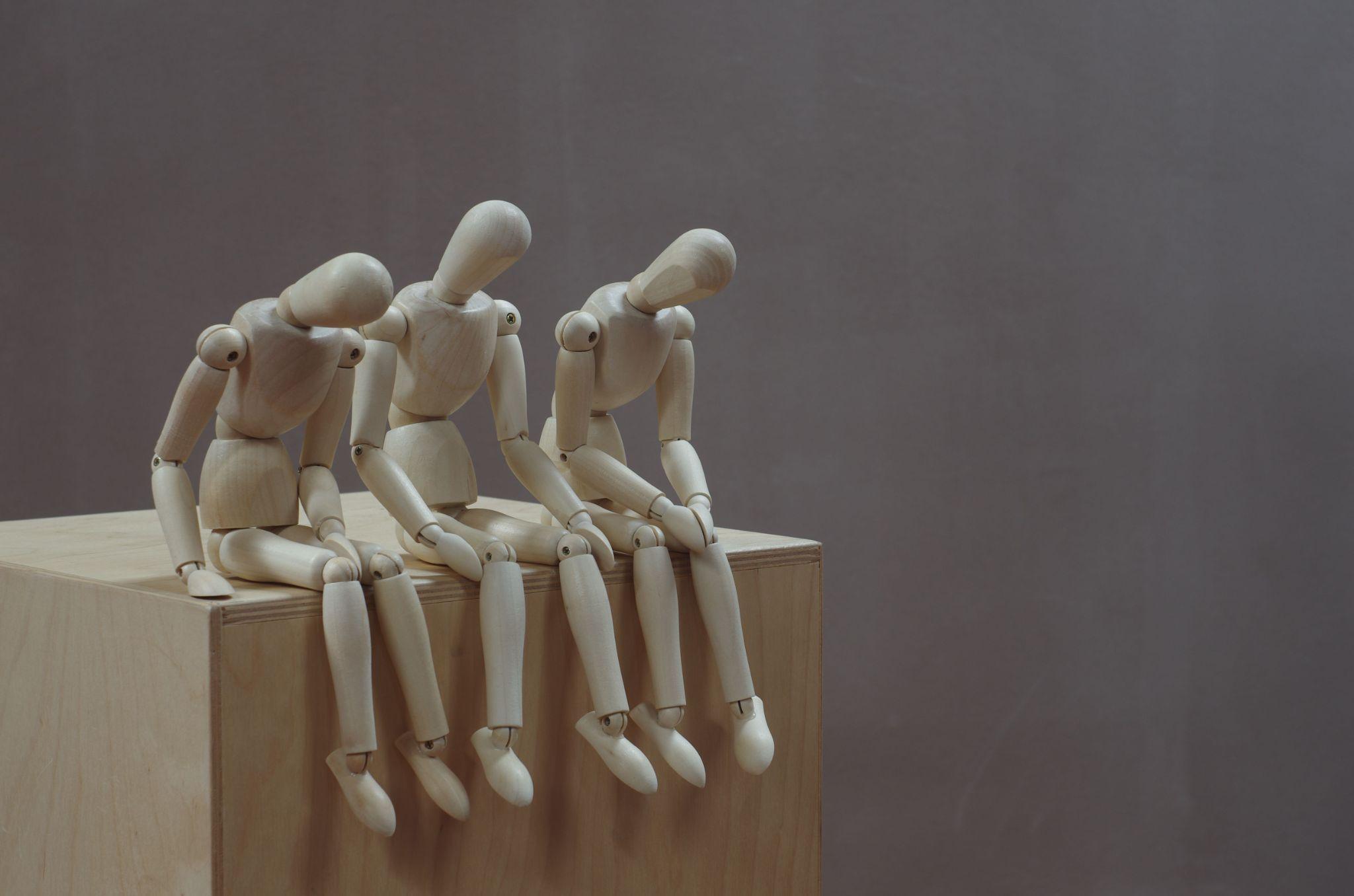 a picture of three wooden jointed poseable figurers sat on a box looking sad and uncomfortable