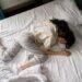 The image shows a lady in pain trying to get comfortable and trying rest she is lying on her bed, her postion indicates she is in great discomfort.