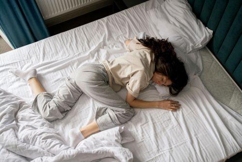 The image shows a lady in pain trying to get comfortable and trying rest she is lying on her bed, her postion indicates she is in great discomfort.